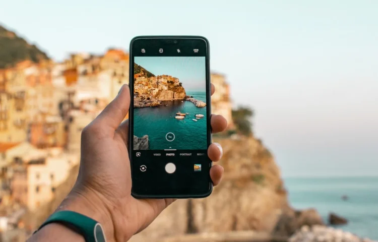 Une main tient un smartphone en train de photographier un village coloré en bord de mer pendant les vacances