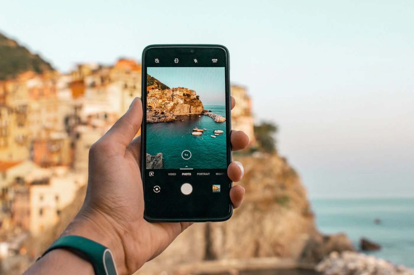 Une main tient un smartphone en train de photographier un village coloré en bord de mer pendant les vacances